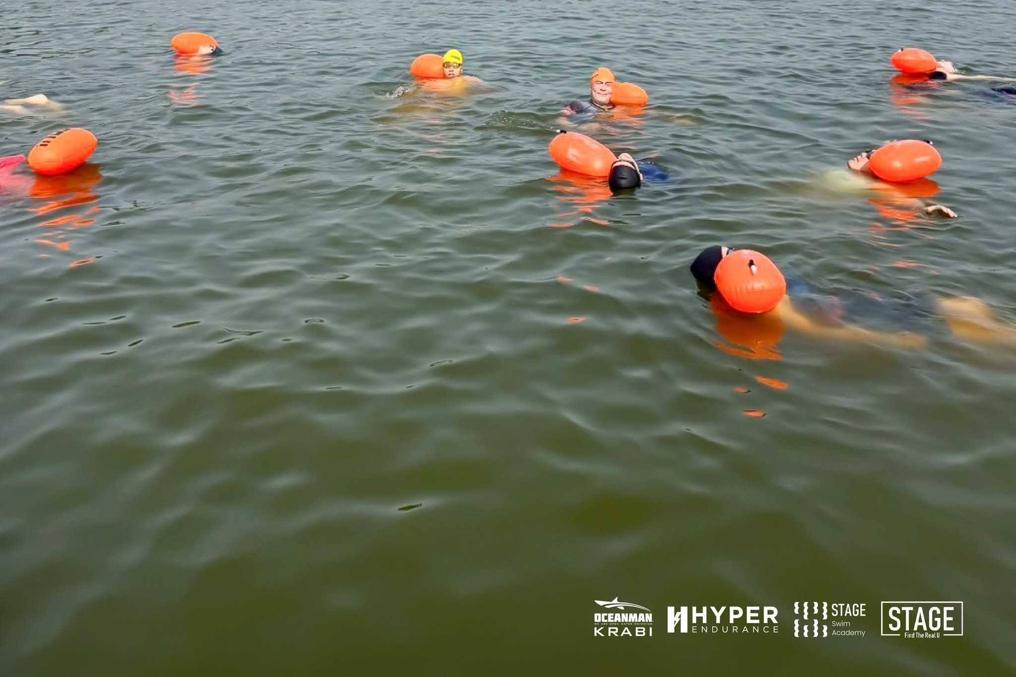 Open water swimmers with orange safety buoys on a lake