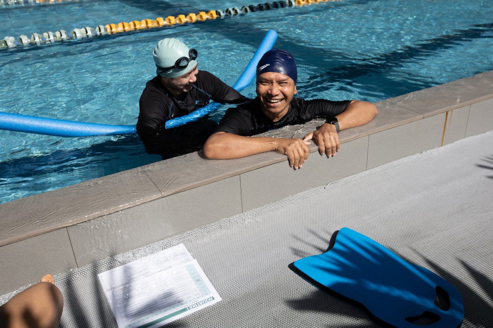 โค้ชและผู้เข้าอบรมที่ขอบสระพร้อมอุปกรณ์ช่วยลอยตัว · Coach and trainee at the pool wall with a float noodle