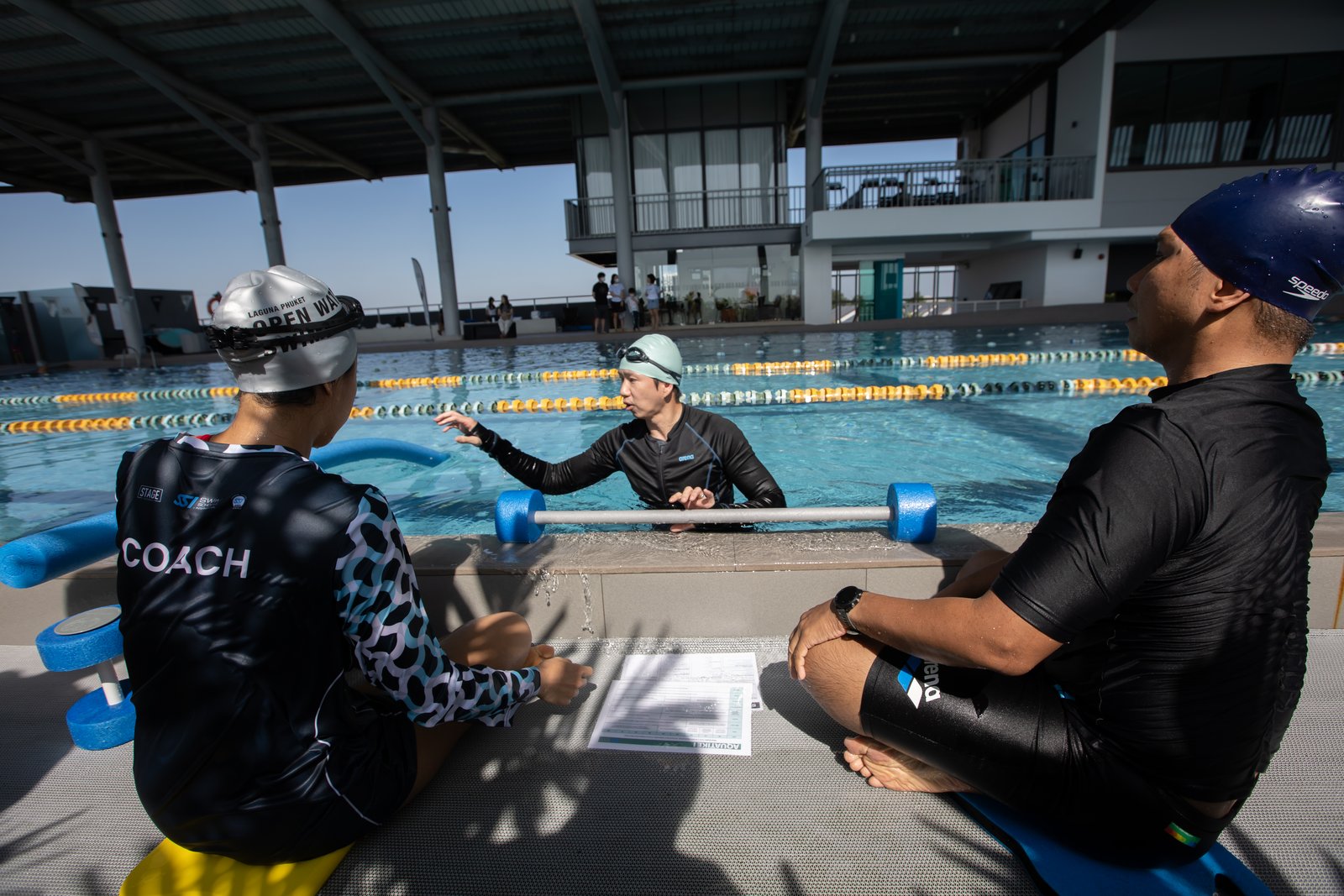โค้ชและผู้เข้าอบรมทบทวนแผนการสอนที่ขอบสระ · Coach and trainee reviewing a lesson plan poolside